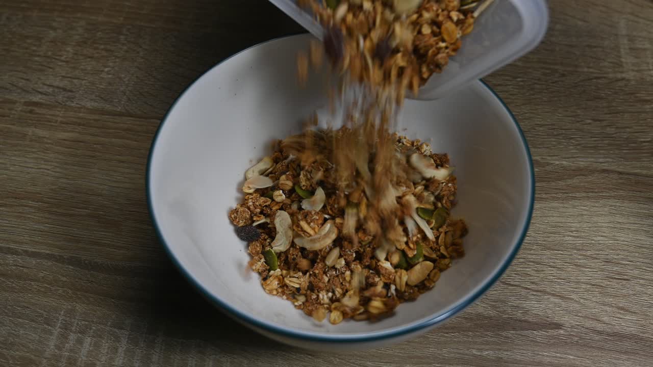 탁자 위에 있는 빈 그릇, 그라놀라가 플라스틱 용기에 건강한 아침 식사의 일부로 부어졌습니다.