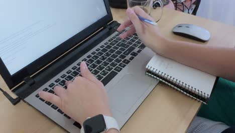 detailed close-up of hands actively writing in a notebook and positioned over a laptop keyboard