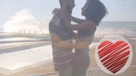 Animation-of-heart-icon-over-african-american-couple-in-love-hugging-on-beach