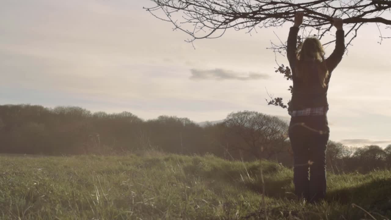 Woman looks out onto landscape under branches of a tree wide shot