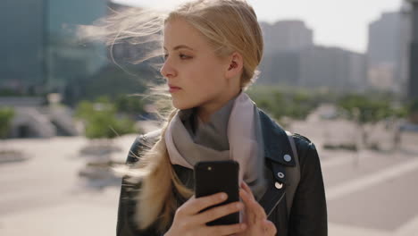 slow motion portrait of cute young blonde woman texting browsing using smartphone social media app in windy urban city background