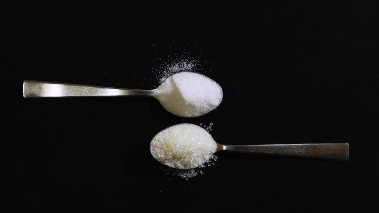 Zucchero semolato e sale da tavola su cucchiaini di metallo che evidenziano il contrasto tra ingredienti dolci e salati