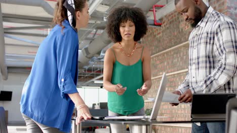 Three-diverse-colleagues-discussing-over-documents-and-laptop-at-office