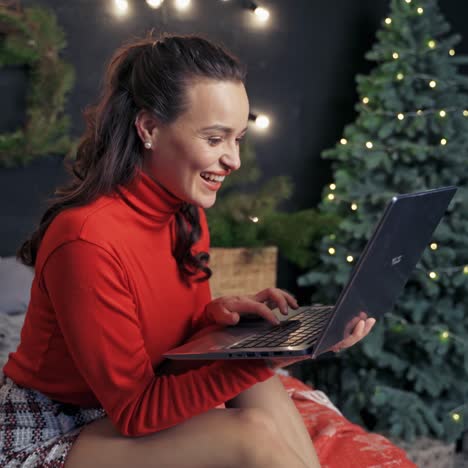 happy woman with gadget on bed at christmas. attractive girl laughing while looking into the laptop on christmas tree background at home.