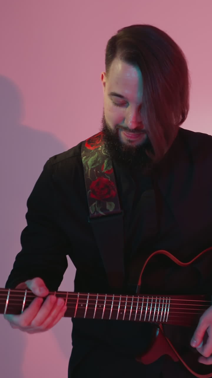 A guitarist in a black outfit stands and plays an electric guitar, moving slowly against a colorful background. The shadows on the wall create a dynamic visual effect
