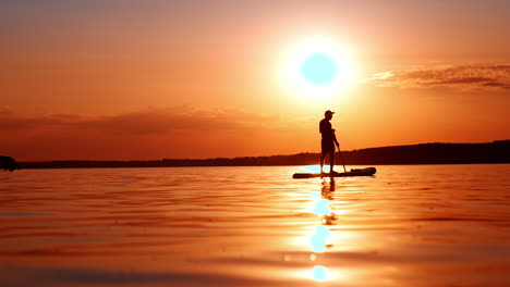 amazing sunset on the calm river. male silhouette stands on the sup board. low angle view.