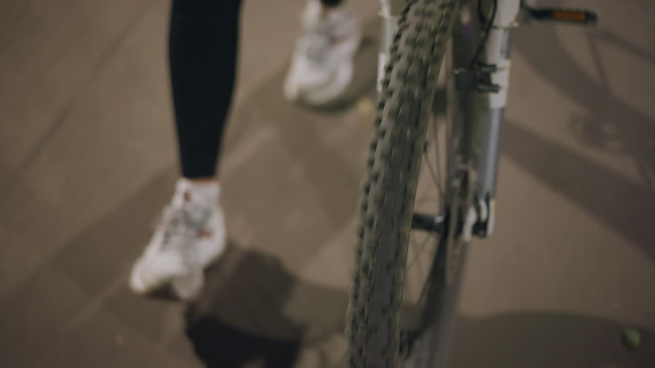 Nighttime Urban Park With Woman And Bike Focus, Caucasian Woman Beside Bicycle In Park During Low Warm Light, Scene Showing Woman Walking With Her Bicycle At Night On Textured Park Pavement