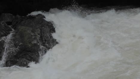 Slow-motion,-rapid-river-whitewater-crashing-against-rock,-flowing-downstream