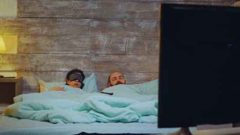 una pareja en el dormitorio se queda dormida frente a la televisión.