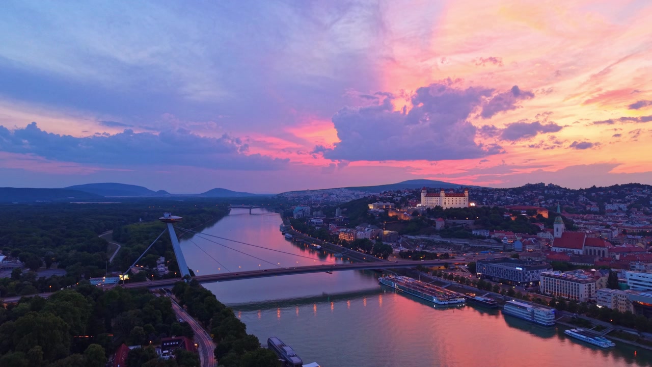 Himmel over Bratislava ved solnedgang. Floden og Bratislavas skyline viser klare farver ved solnedgang med skyer og spejlinger i vandet.
