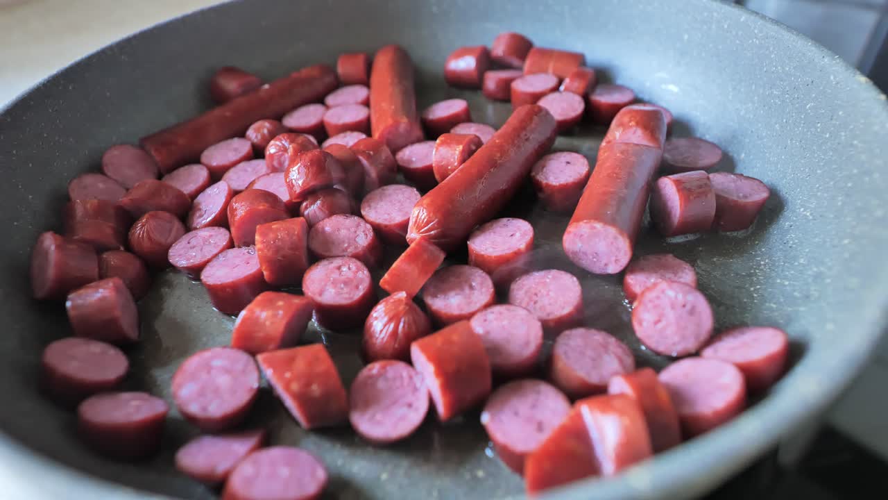 Frying pan full of sausages searing in oil, releasing aroma in home kitchen