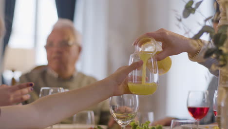 Un-Niño-Sentado-En-Una-Mesa-Festiva-Con-Su-Familia-Mientras-Su-Madre-Vierte-Jugo-De-Naranja-Y-él-Lo-Bebe