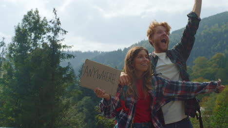 Loving-couple-hitchhiking-nature-on-mountains-road.-Travelers-hold-placard-sign.