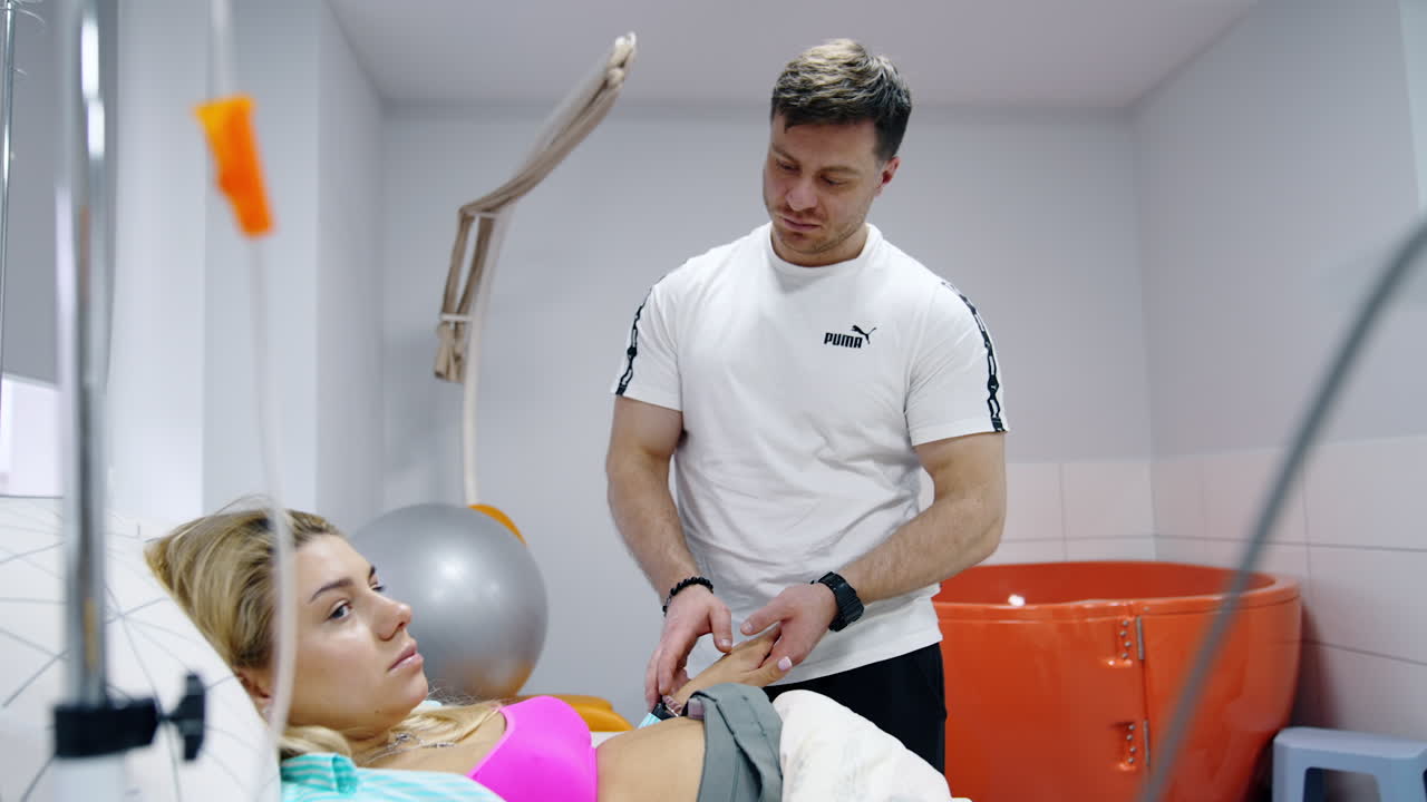 Mid-aged man holding a hand of his wife lying in the hospital bed. Couple expecting a baby to come up.