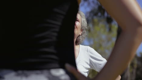 Focused-senior-woman-training-with-personal-couch-in-park.