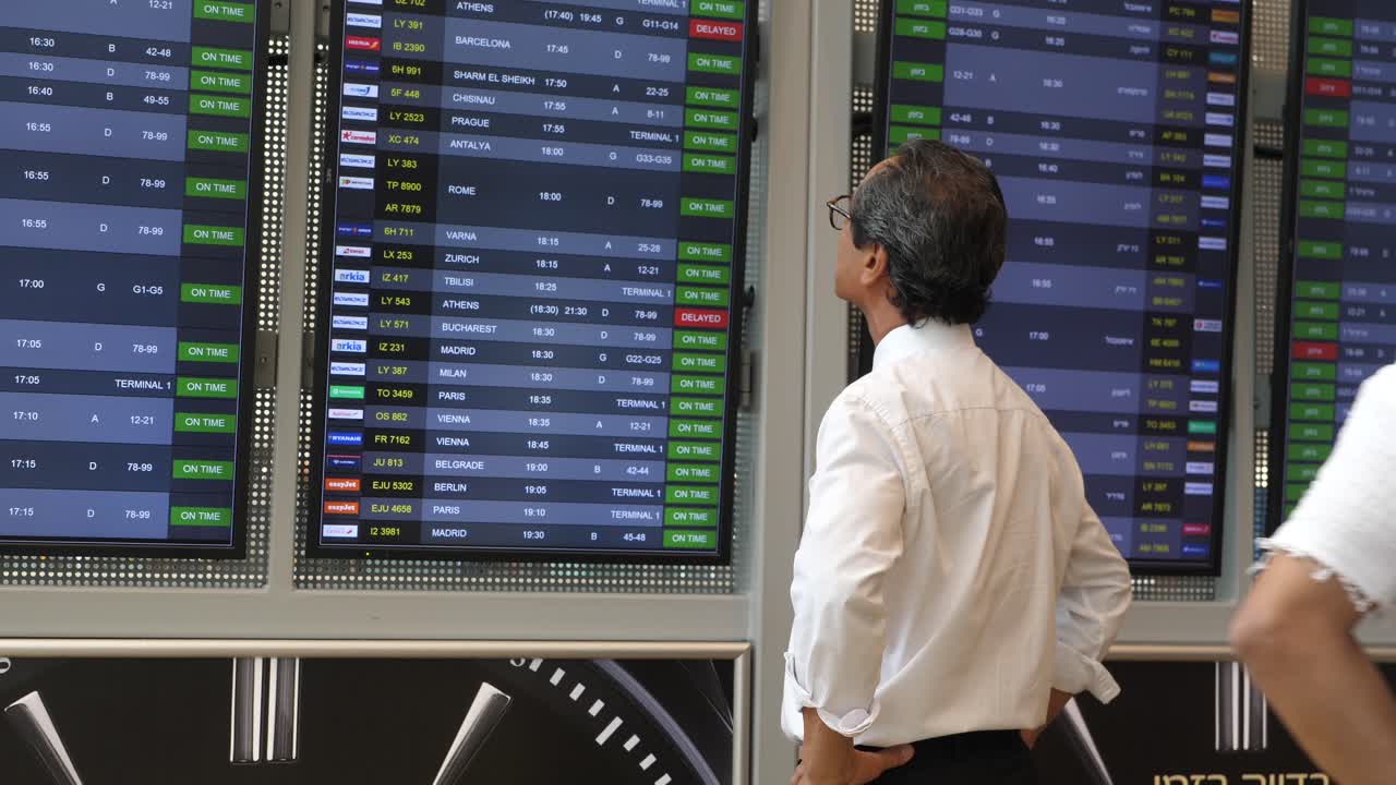 un hombre de negocios japonés se encuentra en el aeropuerto ben gurion en israel, mirando la tabla de llegadas y salidas.