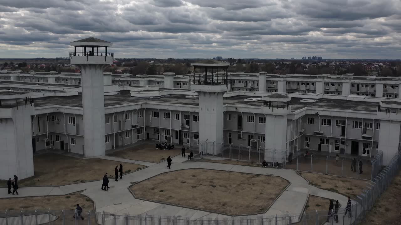 Aerial video of a prison complex with watchtowers under a cloudy sky