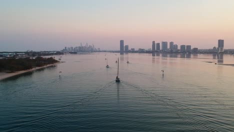 a high view of a group of yachts at sunset entering a harbour with a smoke haze city skyline in the distance