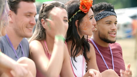 Friends-sit-on-grass-talking-at-a-music-festival,-side-view