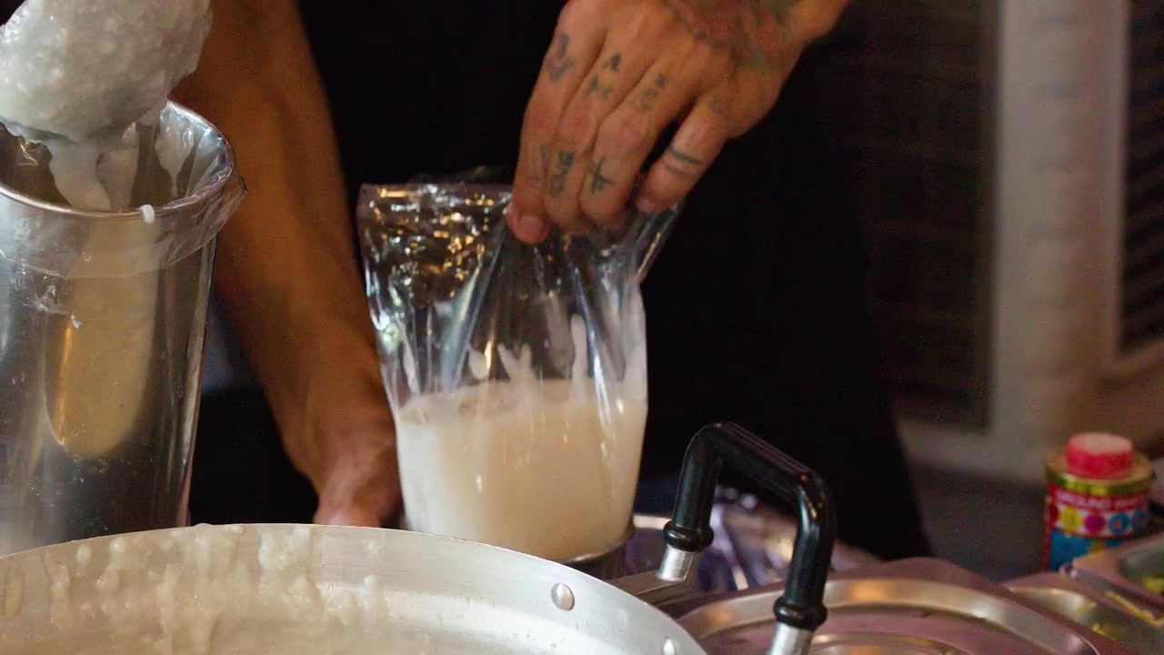 Close-up of a chef ladling hot congee into a plastic bag at a Thai market.