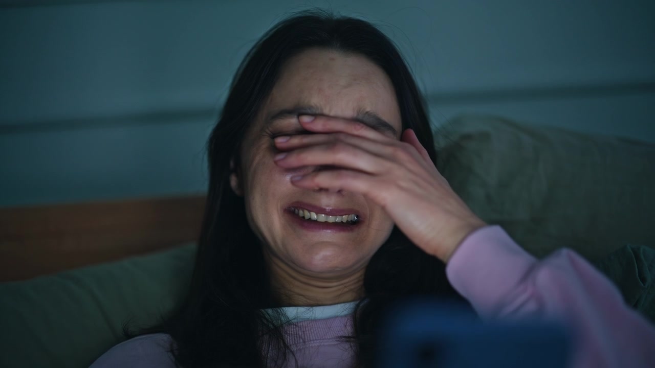 Crying woman watching cellphone lying bed at sleepless night home closeup