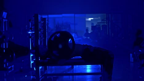 handsome young man doing bench press workout in gym. blue light filter. strong abs. heavy lift. video from the side
