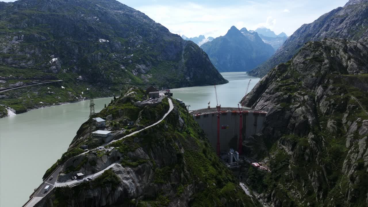 Aerial view showcasing the Grimselsee Lake and dam wall in Switzerland, with construction cranes visible amidst the mountainous landscape. Pedestal Down