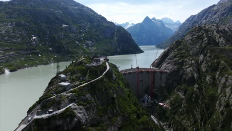 aerial view showcasing the grimselsee lake and dam wall in switzerland, with construction cranes visible amidst the mountainous landscape. pedestal down