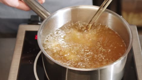 Person-is-frying-chicken-at-home,-using-heated-oil-in-pan-for-deep-frying,-slowly-rotating-and-spinning-it-into-pan