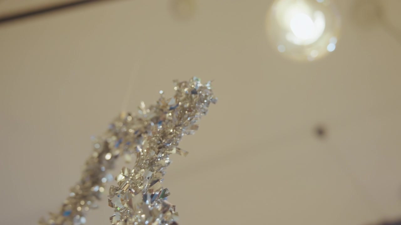 Primo piano di una ghirlanda di tinsel argentato che luccica sotto le calde luci del soffitto, la profondità di campo ridotta cattura scaglie metalliche scintillanti e anelli delicati, atmosfera di installazione da visual merchandiser, elegante e festivo.