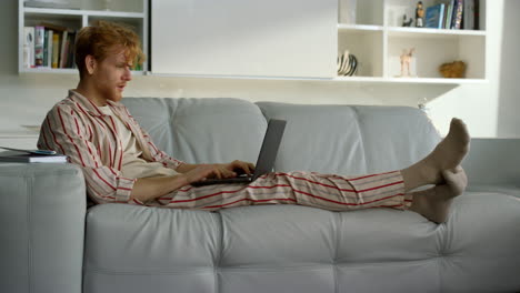 Smiling-man-making-video-call-resting-on-sofa.-Happy-ginger-man-waving-computer