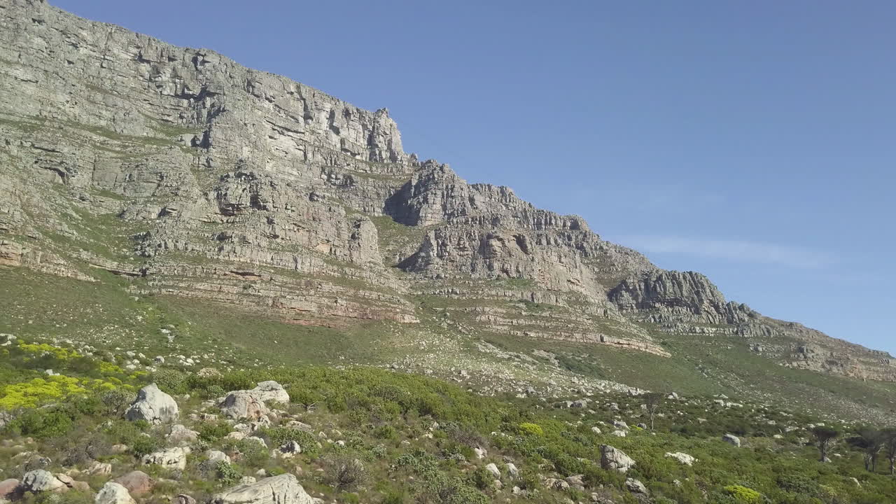 Vista panoramica aerea dal basso con drone della Table Mountain al sole del tardo pomeriggio contro un cielo blu.