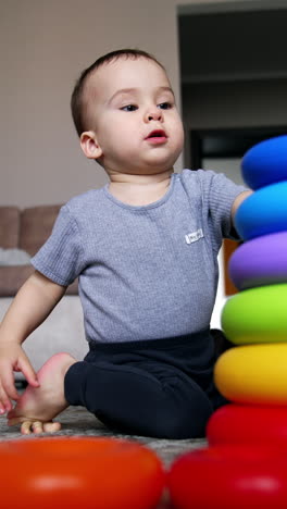 lovely kid takes the rings of pyramid from the floor. toddler constructs pyramid and learns size and colors. low angle view. vertical video