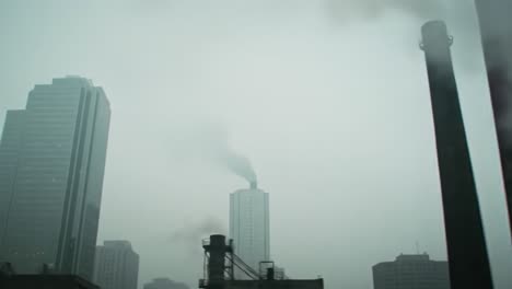 a gloomy urban landscape shrouded in fog and pollution with towering buildings and rising smoke emitting from industrial structures