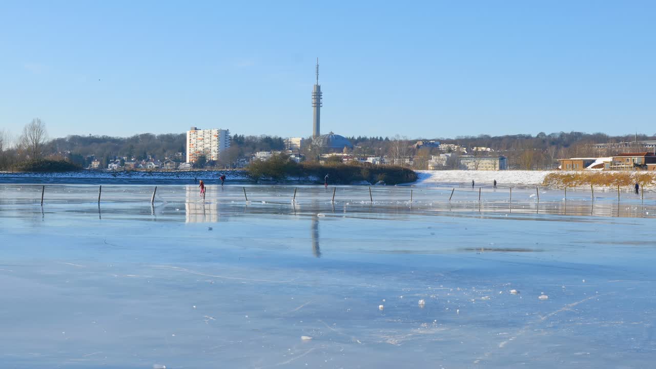 People Ice Skating on a Frozen Lake with a City Skyline and Tower in Winter