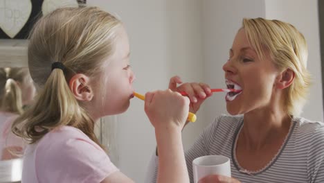 vista lateral de una mujer caucásica y su hija cepillándose los dientes