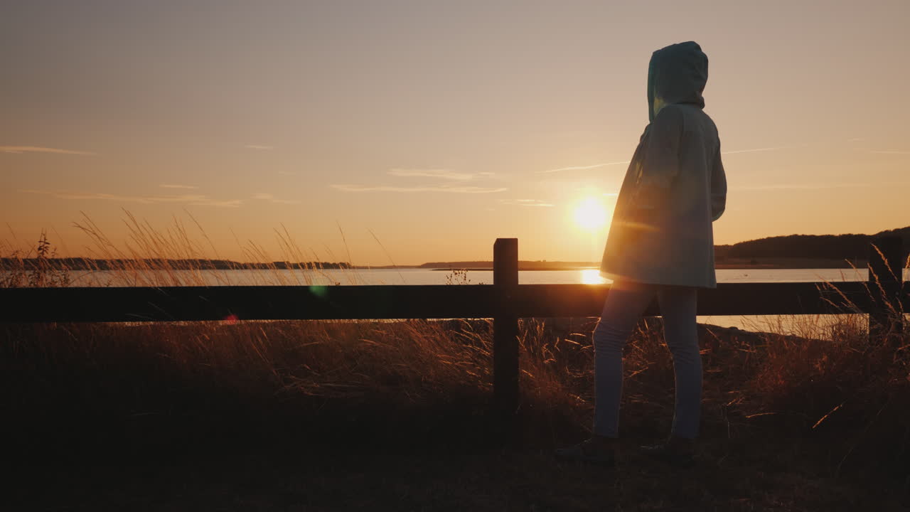 호수 위로 일몰을 감상하는 울타리 옆에 앉아 외로운 여자 실루엣