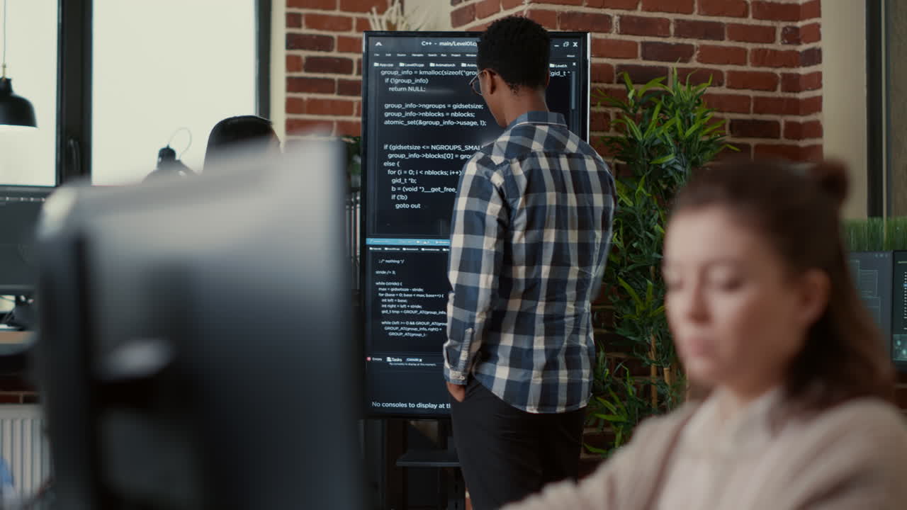System developers analyzing code on wall screen tv looking for errors comparing results on digital tablet