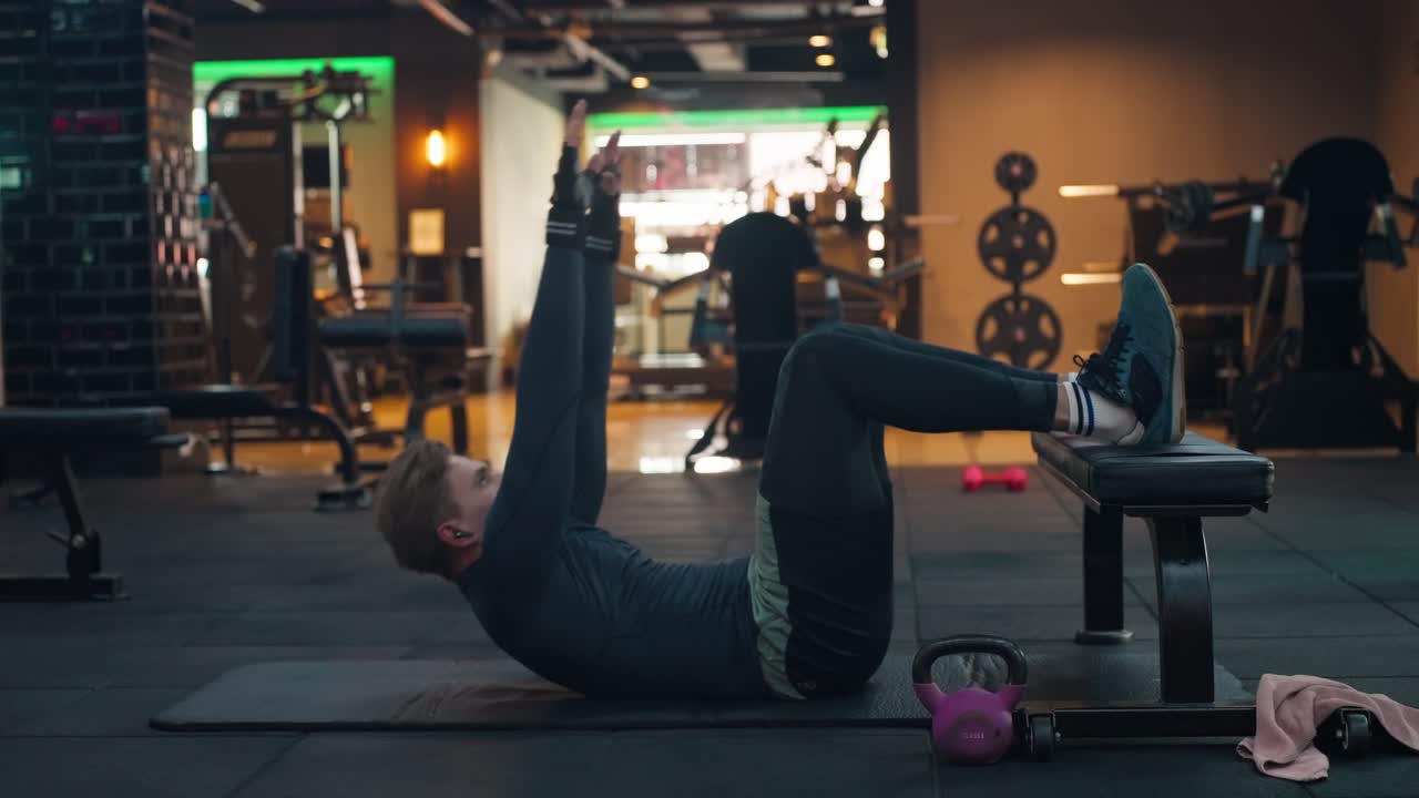 Caucasian man exercises on a yoga mat at gym. Male fitness model performing abs crunch at fitness center - side view