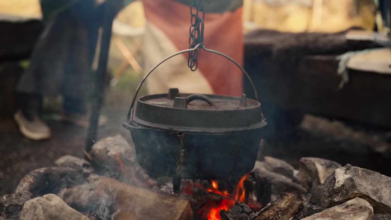Dutch oven cooking over an open campfire with flames touching the pot and smoke curling upward