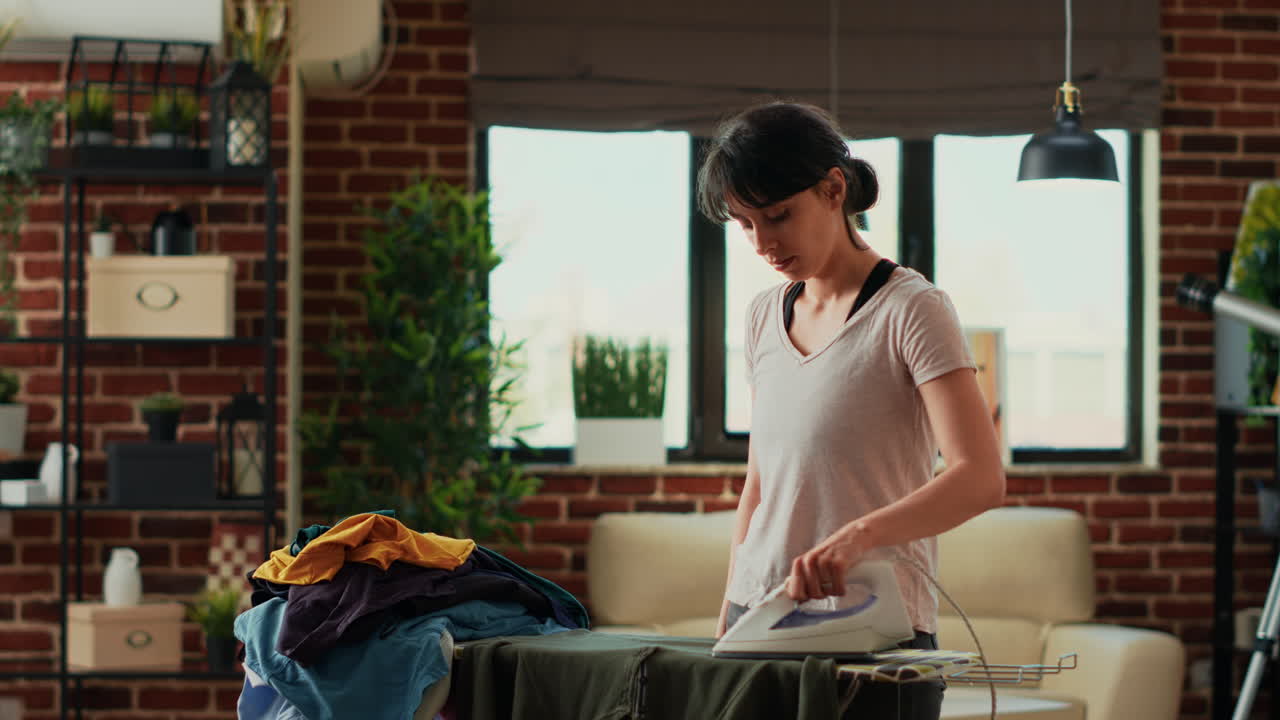 Young adult using steam iron to smooth out wrinkles on clothing