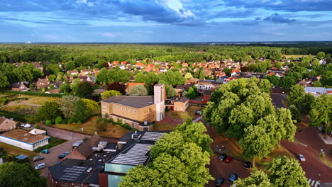 tranquil village amid trees. aerial view of a tranquil village with greenery, houses, and a church under a clear sky