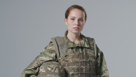 studio portrait of serious young female soldier in military uniform against plain background