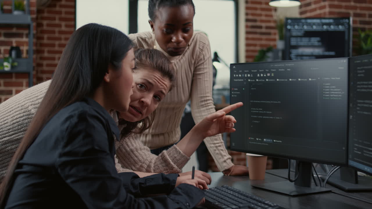 Programer pointing at computer screen explaining running code to coworkers brainstorming software ideas