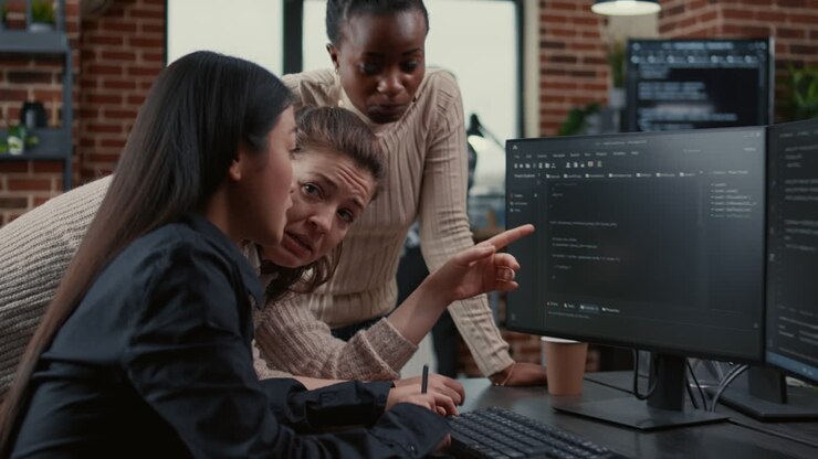 Programer pointing at computer screen explaining running code to coworkers brainstorming software ideas