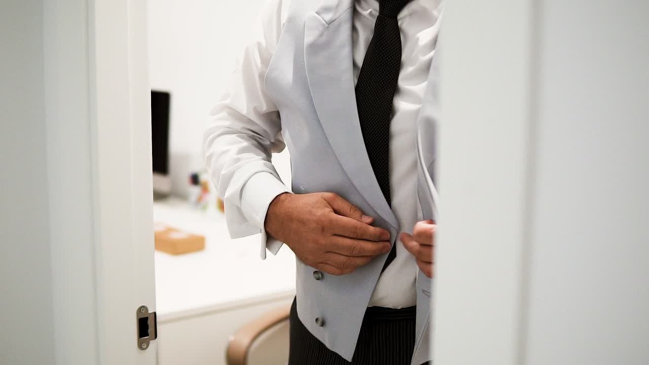 el novio en su día de bodas atando su elegante traje gris, de pie en el baño preparándose