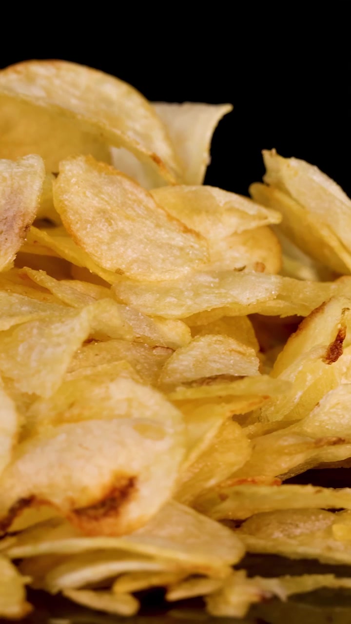 Crispy potato chips rotate and zoom out against black background, revealing texture and golden color