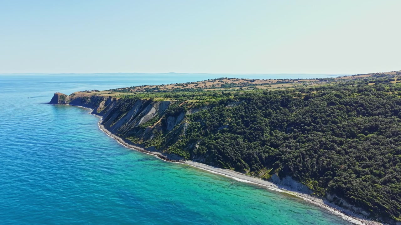 Vista di una zona costiera con scogliere, alberi e acqua blu di giorno sotto un cielo limpido.