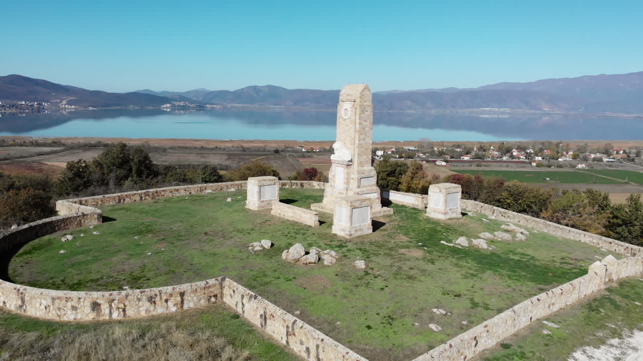 Ripresa drone grandangolare del Memoriale di Doiran nella Grecia settentrionale, con una statua di leone in marmo, una corona commemorativa e nomi di soldati incisi, con il Lago Doiran e le montagne in lontananza