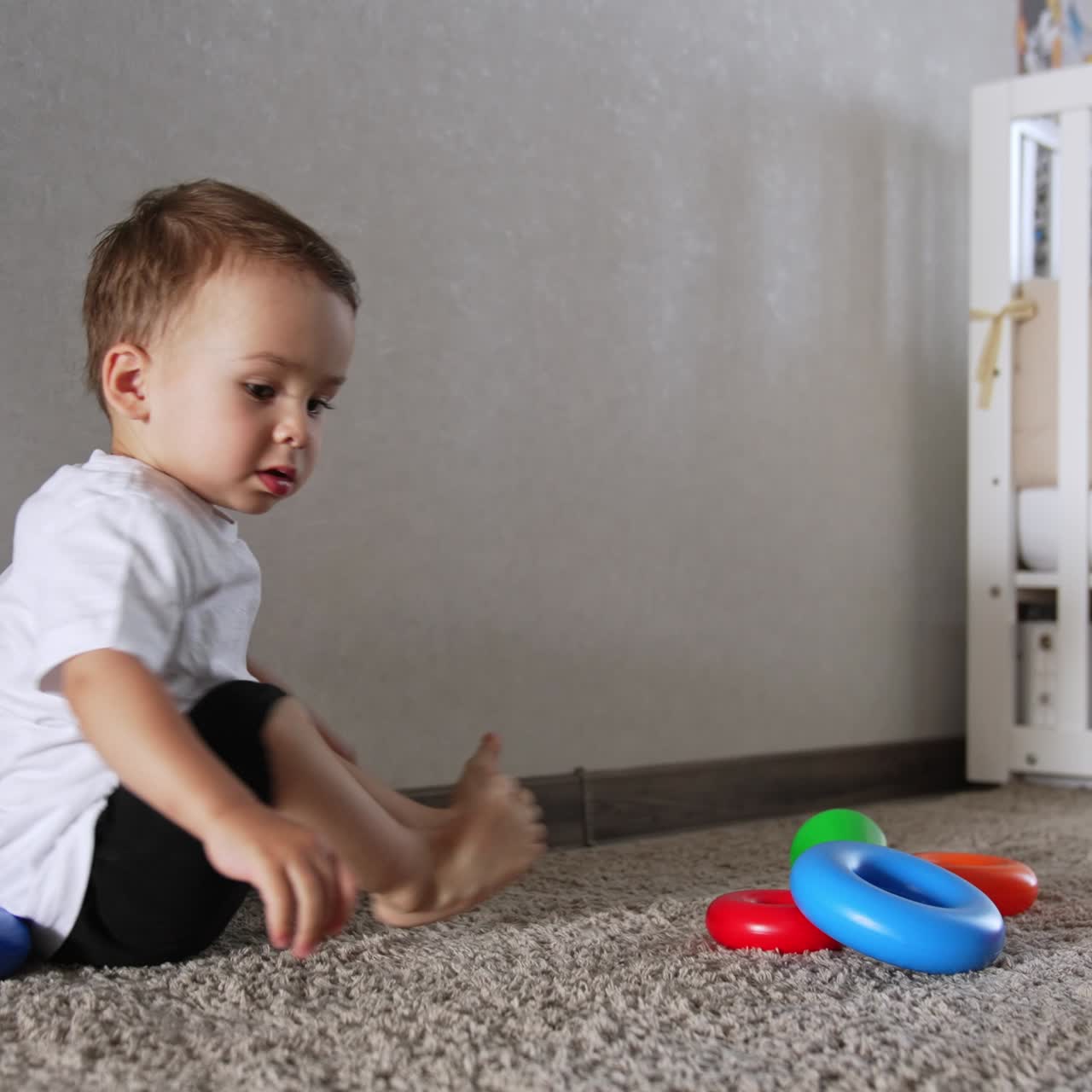 Caucasian baby boy played with toy pyramid on the floor. Kid turned to camera and then ran away